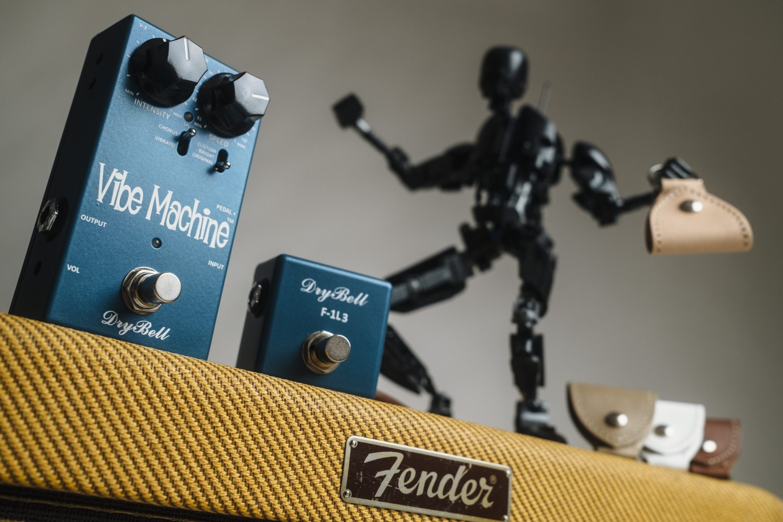 DryBell Vibe Machine V-3 guitar pedal with F-1L3 footswitch on tweed amp, alongside leather keychain pick holders.